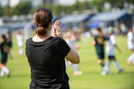 Asian parents watching and supporting their children playing football on a sunny afternoon at a local community tournament.
