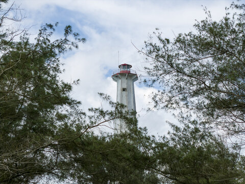 Aerial view of a towering lighthouse, its white structure piercing the sky framed by lush green foliage, Mercusuar Samas, Bantul Regency, Indonesia.