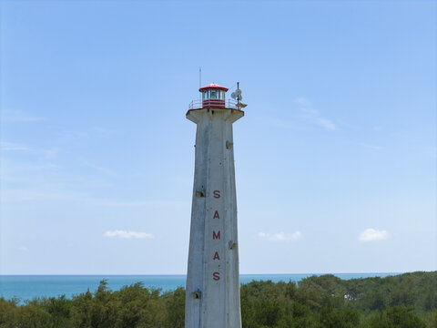 Aerial view of the stark white lighthouse named "SAMAS" rising against the azure sky and the turquoise sea, Mercusuar Samas, Bantul Regency, Indonesia.