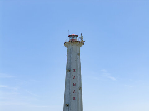 Aerial view of the stark white lighthouse, 'SAMAS' etched vertically, piercing the clear blue sky, a beacon of maritime guidance, Bantul Regency, Daerah Istimewa Yogyakarta, Indonesia.