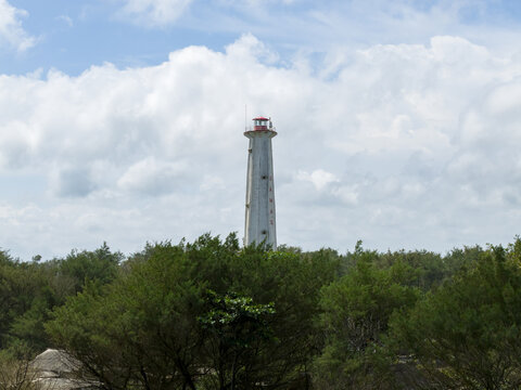 Aerial view of a striking lighthouse piercing the horizon, contrasting against the lush green canopy and a backdrop of a cloudy sky, Bantul Regency, Daerah Istimewa Yogyakarta, Indonesia.