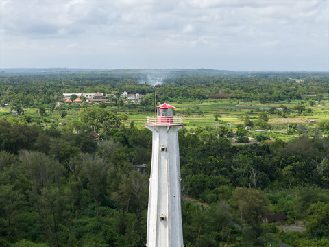 Aerial view of the stark white lighthouse piercing through a verdant canopy, a beacon against the backdrop of the lush landscape, Bantul Regency, Daerah Istimewa Yogyakarta, Indonesia.