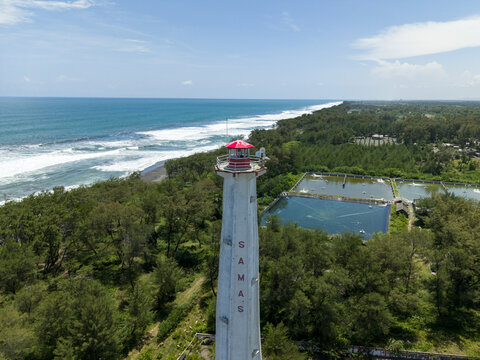 Aerial view of the towering Mercusuar Samas lighthouse standing proud against the backdrop of the turquoise ocean and lush greenery, Bantul Regency, Daerah Istimewa Yogyakarta, Indonesia.