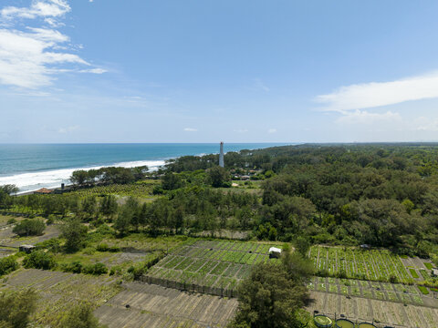 Aerial view of the lighthouse standing tall amidst lush greenery where the land meets the vast ocean, Mercusuar Samas, Bantul Regency, Indonesia.