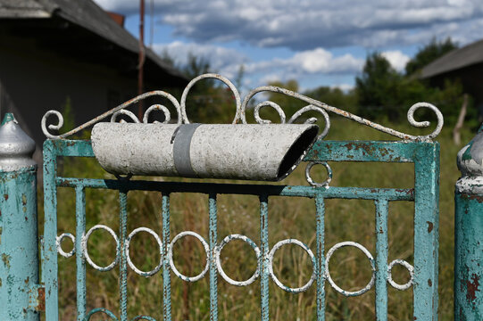Rusty gate with a rolled letter holder attached seen in a rural area during daytime