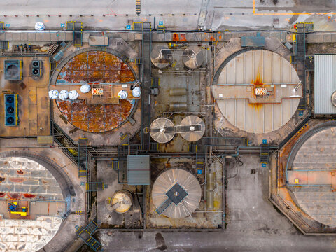 Aerial view of circular industrial structures with weathered surfaces and intricate pipe networks creates a symphony of rust and concrete, Avezzano, Abruzzo, Italy.