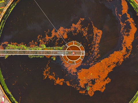 Aerial view of the circular settling tank with bridge and contrasting orange and green residues floating on the dark water, Avezzano, Abruzzo, Italy.
