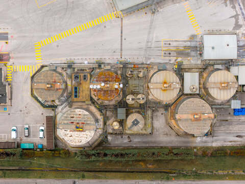 Aerial view of industrial tanks gleaming under the sunlight, juxtaposed against the geometric precision of yellow lines and concrete expanses, Avezzano, Abruzzo, Italy.
