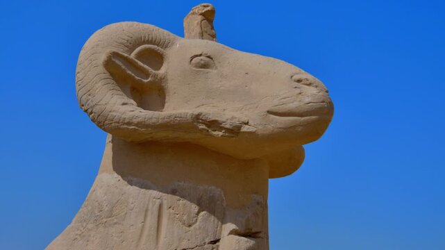 Karnak Temple in Luxor, Egypt. Ancient ram-headed Amun sphinx statue on pedestal at Karnak Temple Luxor Egypt. Stone sculpture against vivid blue sky. Authentic travel and history content.