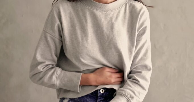 Woman in a hoodie holding and rubbing her stomach showing severe stomach pain