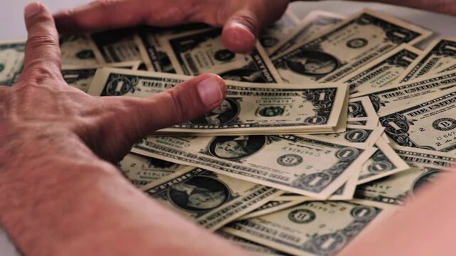 Man raking a huge pile of one‑dollar bills with his hands