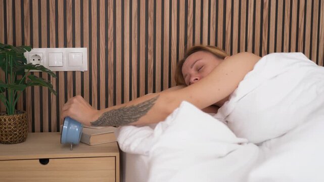 Sleepy woman turning off alarm clock in morning, feel tired and annoyed by loud sound, want to sleep more and stay in cozy bed.Restless sleep and insomnia concept, tired female