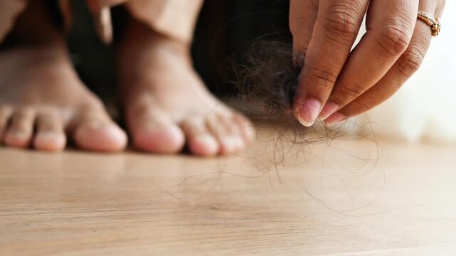 Woman picking up clump of fallen hair from floor, hair loss problem