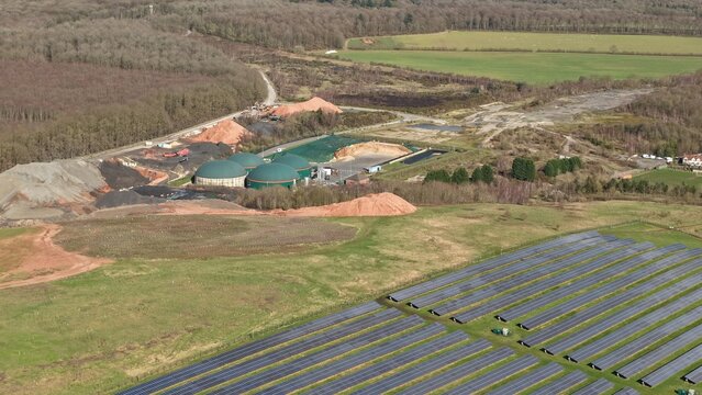 Aerial view of solar panels glinting under the sun, juxtaposed with the rounded green biogas plant against a backdrop of the quaint Meden Vale, Meden Vale, United Kingdom.