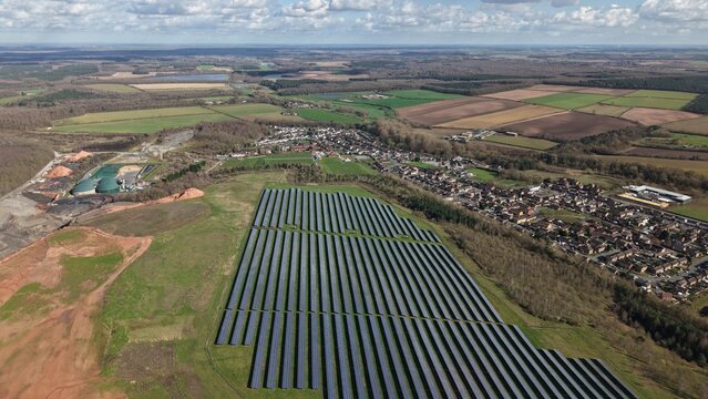 Aerial view of solar panels gleaming under a vast sky, juxtaposed with the quaint town of Meden Vale nestled amidst the verdant landscape, Meden Vale, United Kingdom.