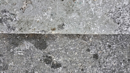 A close-up of weathered concrete divided by a horizontal seam. The grey surface features a gritty,...