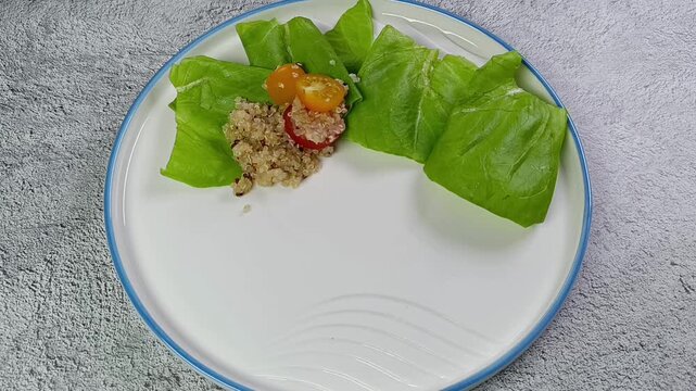 A salad with quinoa, cherry tomatoes, and lettuce is served on a white plate on a gray table. Healthy eating concept. Lenten dish