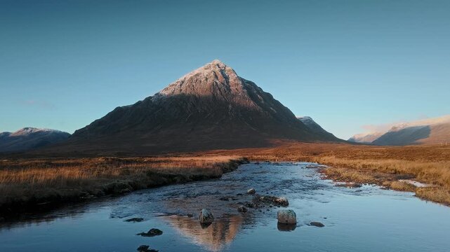 Drone video moving forward above the river toward a mountain in the Scottish Highlands with calm reflection golden light and remote wilderness scenery