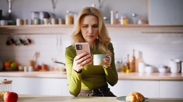 Focused woman using smartphone sitting breakfast table enjoying coffee closeup