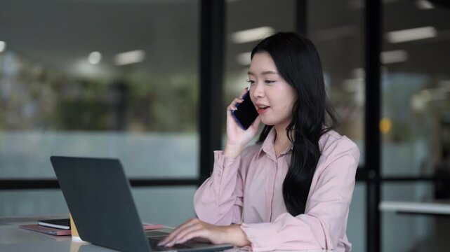 Asian adult woman focused on laptop in modern office space using technology to work online managing business projects professionally