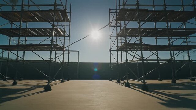 真昼の強い太陽の下、コンクリートの地面に鋭い影を落とす複雑な足場