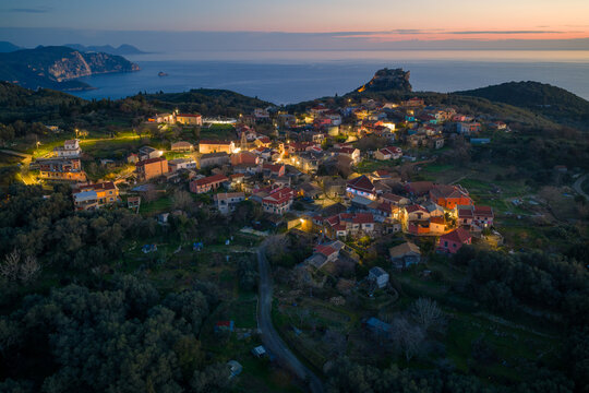 Drone shot of traditional Krini village and Byzantine Angelokastro castle at sunset with orange sky and green olive groves in Corfu island Greece