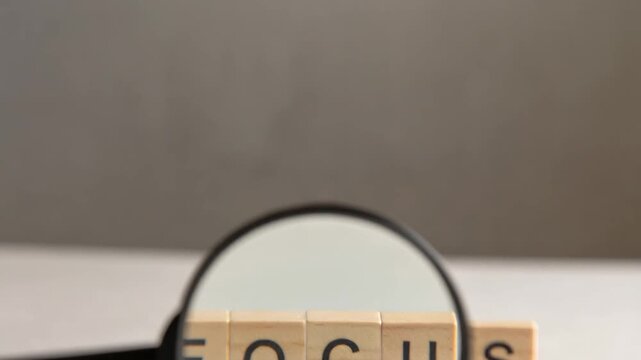 Magnifier emphasizing word FOCUS on wooden blocks showing mindset and personal development concept