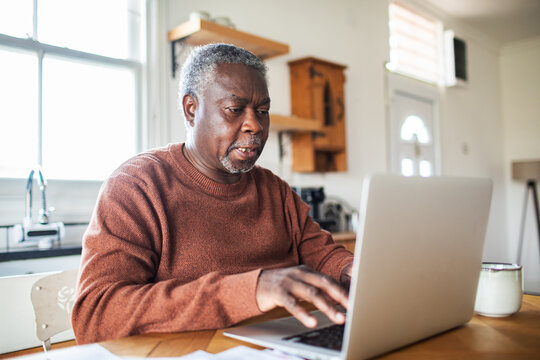 Senior man working on laptop at home kitchen table
