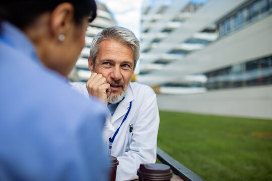 Senior doctor chatting with colleague outdoors at hospital campus