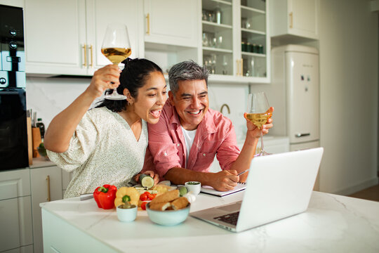 Cheerful couple toasting wine during online cooking class in modern kitchen
