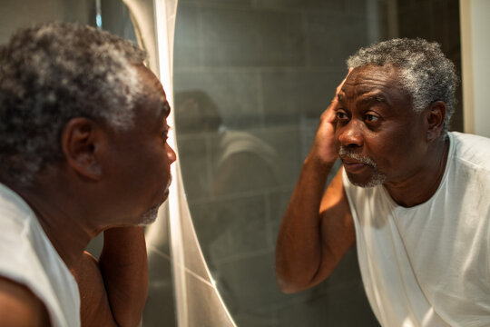 Senior man examining his hair in bathroom mirror