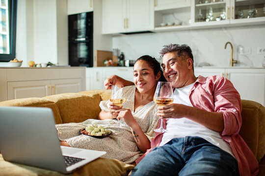 Happy couple watching laptop and drinking wine on sofa at home