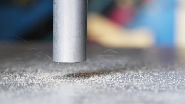 Quartz sand pouring from an aluminum pipe onto a metal surface. Grains bounce and scatter, emphasizing texture and motion.