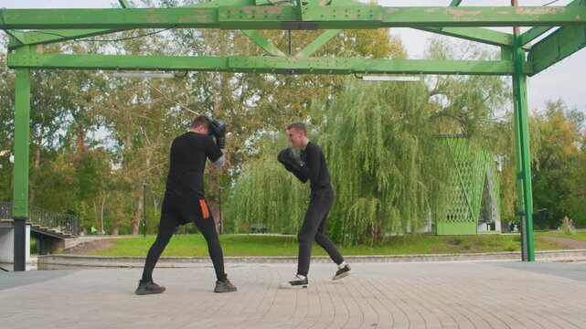 outdoor park boxing exchange between two men, fastpaced counter and slip drills beneath green metal pergola lively footwork, rapid counters, playful rivalry and focused training in autumn park