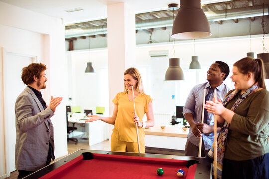 Diverse coworkers playing pool in modern office breakroom