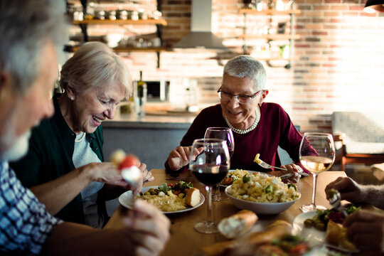 Senior friends enjoying dinner together at home kitchen