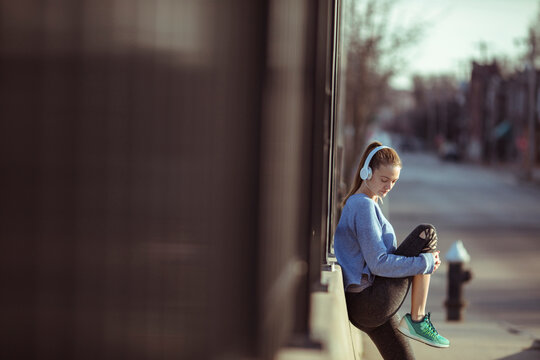 Young woman in athletic wear listening to music on city sidewalk