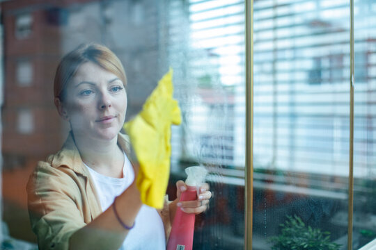 Young woman cleaning window with spray at home