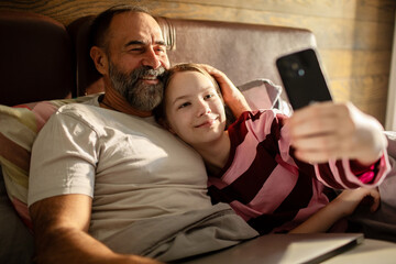 Fototapeta premium Father and daughter taking selfie in bed at home