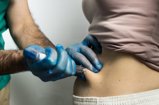 Close-up of a medical professional administering a subcutaneous injection using an injector pen into the patient's stomach area.