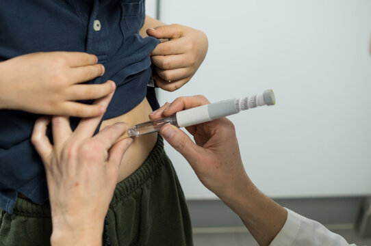 Over-the-shoulder view of a physician injecting a patient in the stomach using a modern medical pen, focusing on the clinical interaction.