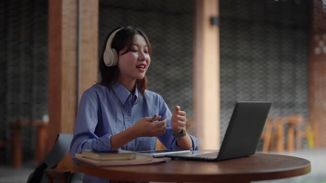 Asian young adult woman remote working online laptop headphones virtual meeting digital education cafe workspace studying business communication