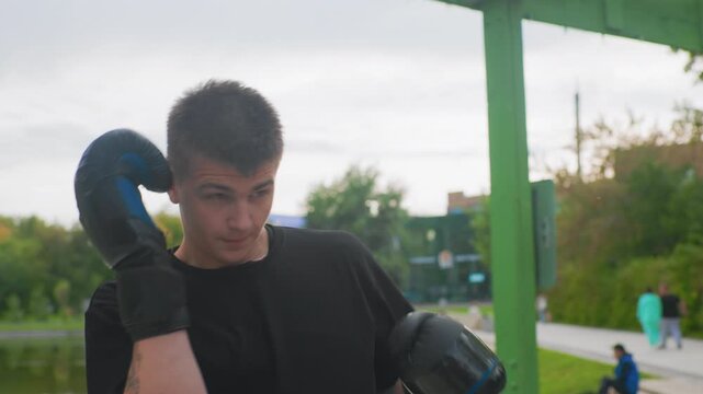 Tense caucasian trainee defends with gloves, highguard protection and tight elbows, focused gaze and quick reflexes, coachguided counter drills on riverside walkway, trees and lake backdrop,