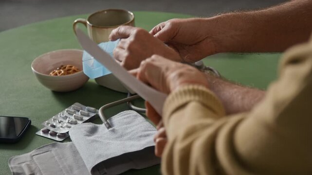 Close-up view of unknown man sorting capsules holding blue plastic pill organizer and closing lids of compartments while wife studying prescription