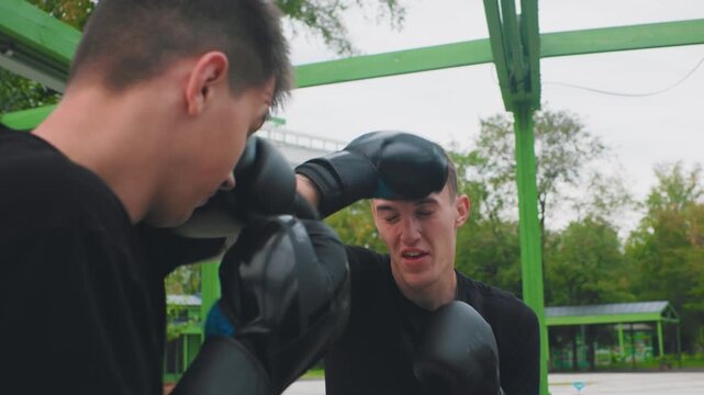 Trainer gives tactics outdoors, Young coach provides boxing strategies beneath green pavilion, Tactic instruction delivered by young coach to partner outdoors with keen eye contact