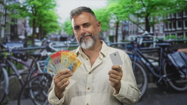 Man holding swiss franc banknotes fanned in one hand and a card in the other with bare hands on street in amsterdam; wealth confidence.