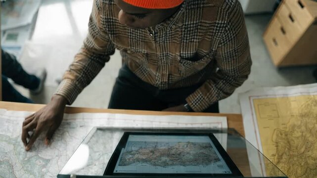 Overhead shot of a document specialist using an overhead scanner for large format maps focused scanner glass and digital screen with outoffocus workspace.