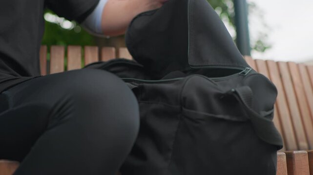 white person rummages through black duffel bag on bench, lifting liner and scanning pockets to grab water bottle quick hands, green background, urban commute vibe frames show runner grabbing