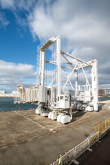 Fototapeta premium Large white mobile passenger boarding bridge at a seaport harbor pier. Industrial maritime gangway for cruise ships at a terminal under a blue sky. Modern shipping infrastructure by the ocean.