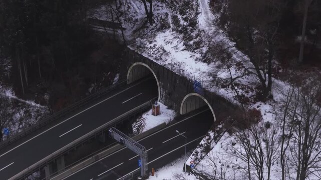 Aerial view in Innsbruck, Austria shows twin stone arch tunnels, elevated roads, blue EU signs, and a yellow DISCORDIA freight truck moving toward a portal in snow.